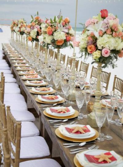 Destination Event Chic reception in Destin Florida. Farm tables with gold chiavari chairs, gold chargers, white plates,…