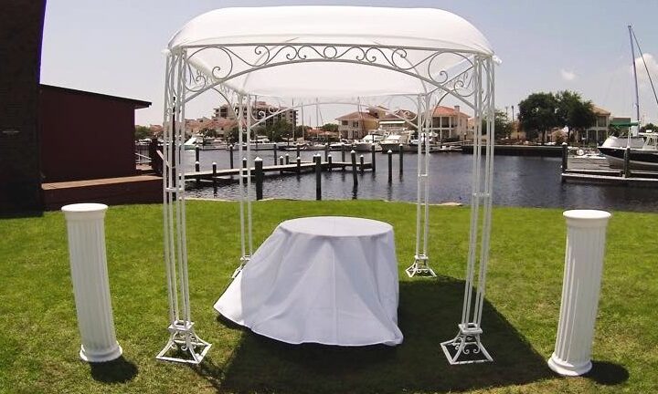 White metal arbor chuppah with draped columns on a waterfront lawn