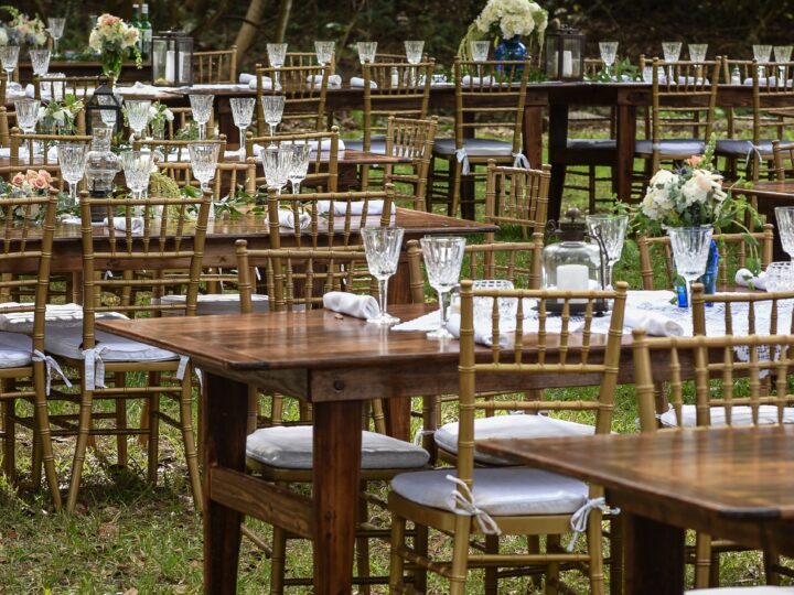 Wooden farm tables with Chiavari chairs, glassware and florals for an outdoor reception